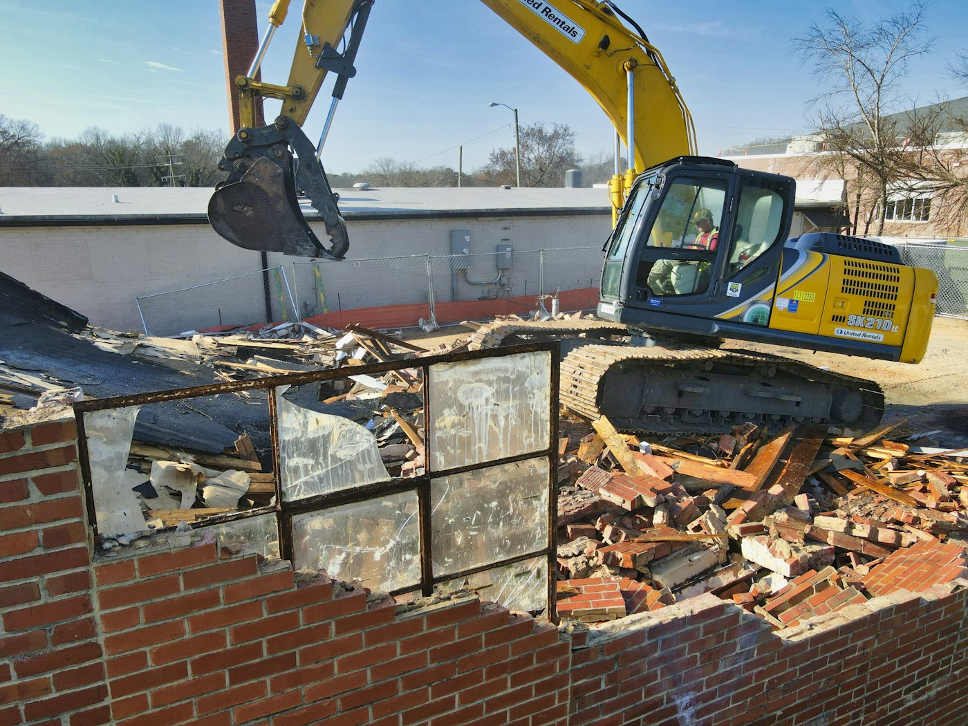 An excavator demolishing an old building to make room for something new — representing Amazon tearing down Q Developer to build Kiro