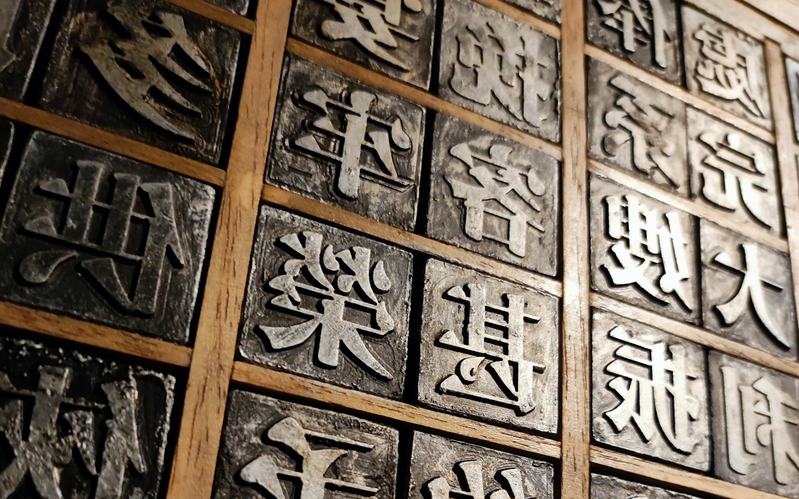 A grid of metal letterpress type blocks set into wooden compartments — each slot a defined, typed character, the analog ancestor of structured output.