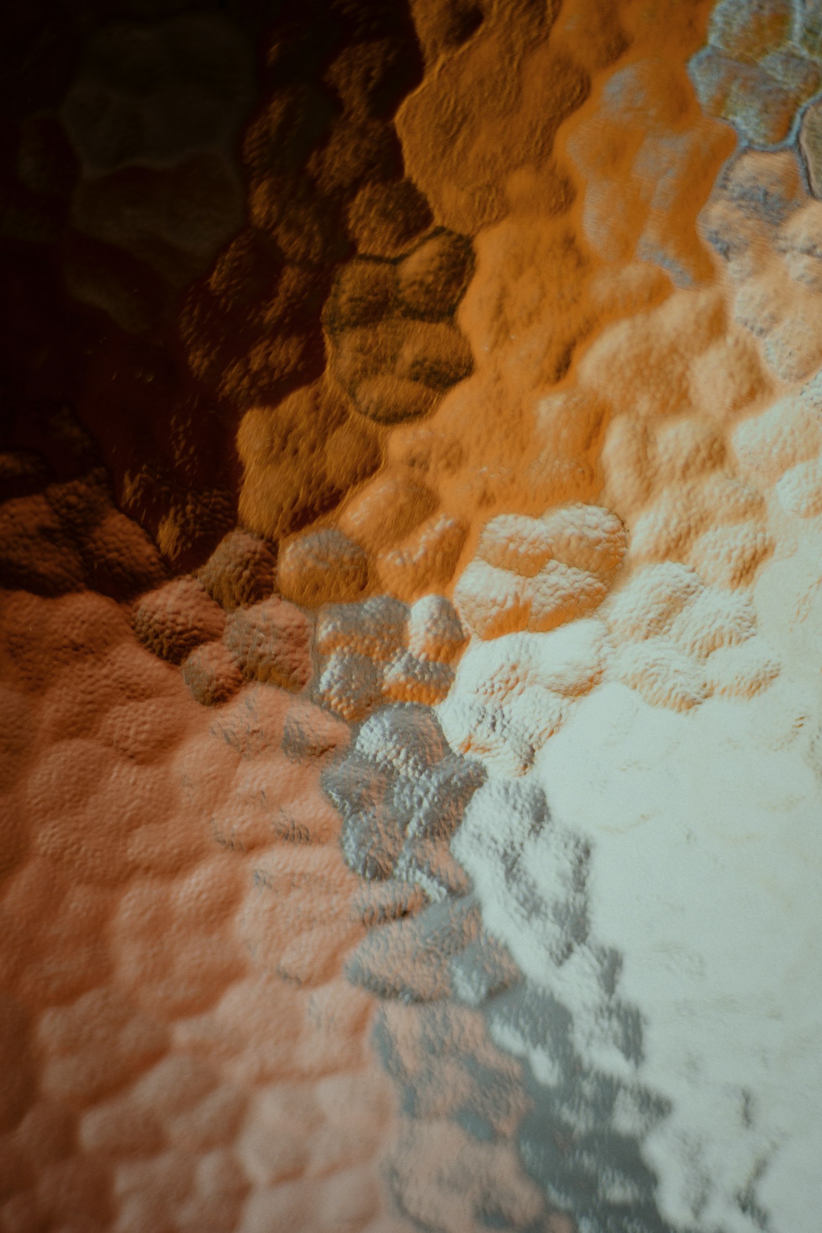 Close-up of textured, refractive glass with warm amber-to-cream tones — the real-world material Apple's Liquid Glass design language imitates on screen.