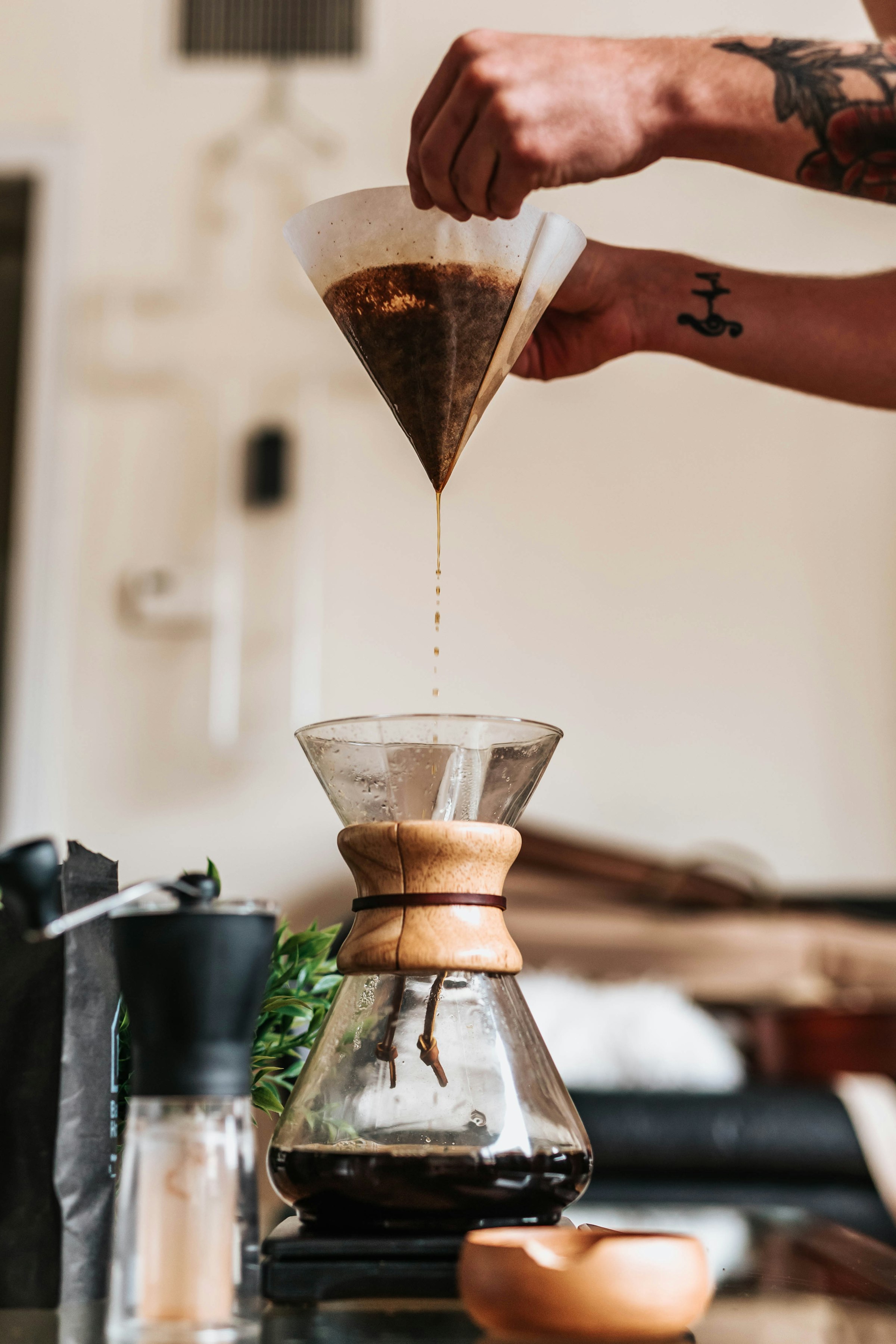 A hand squeezing the last drips of coffee from a paper filter into a Chemex — the kind of multi-minute brew that's worth glancing at from the Lock Screen instead of standing over.