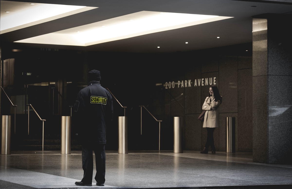 A security guard in a dark uniform standing alert on a grey floor, arms at their sides.