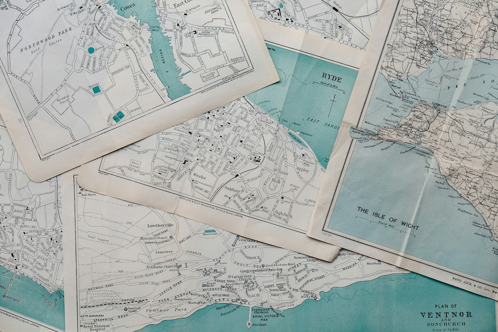 A flat lay of overlapping vintage paper maps at different scales — local town plans layered under a wider regional survey of the Isle of Wight.