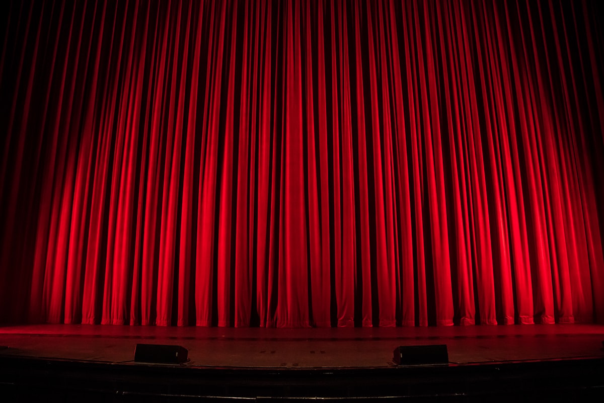 A dramatic red theater curtain on an empty stage — symbolizing Tim Cook's final WWDC keynote curtain call before handing the CEO role to John Ternus